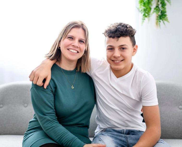 Smiling mother and teenage son sitting together on a couch, showing warmth and close family connection