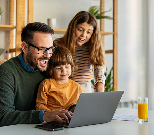 Smiling father and two children sitting at a table looking at a laptop together in a bright room