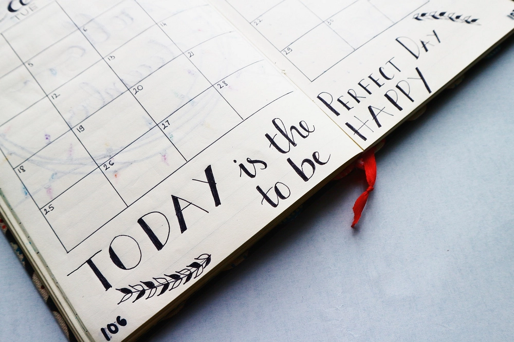 Open planner showing calendar and handwritten quote that reads ‘Today is the perfect day to be happy