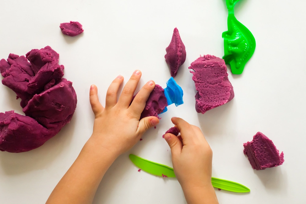 Child playing with purple modeling clay and colorful plastic tools
