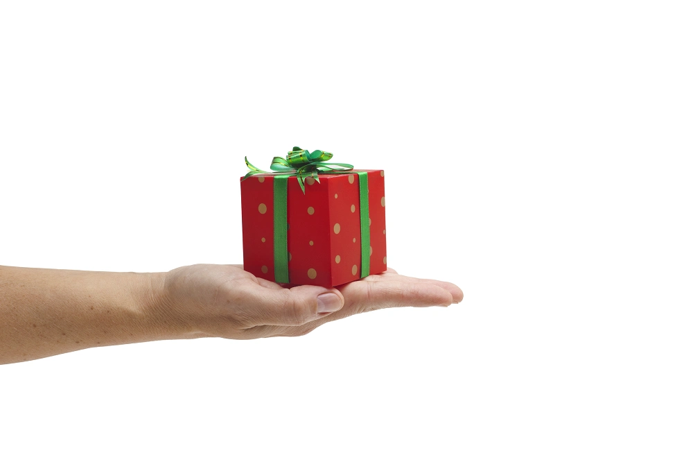 Hand holding a small red gift box with green ribbon and bow on a white background
