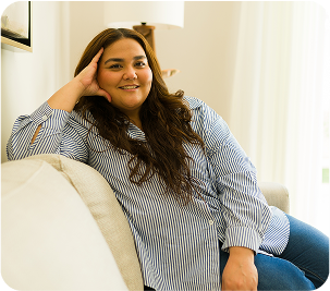 Woman with long brown hair smiling while sitting relaxed on a couch in a bright living room