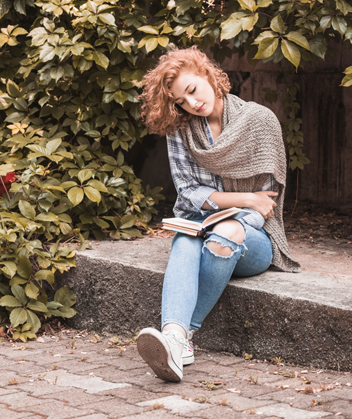 Young woman sitting outdoors reading a book, symbolizing reflection, peace, and personal growth