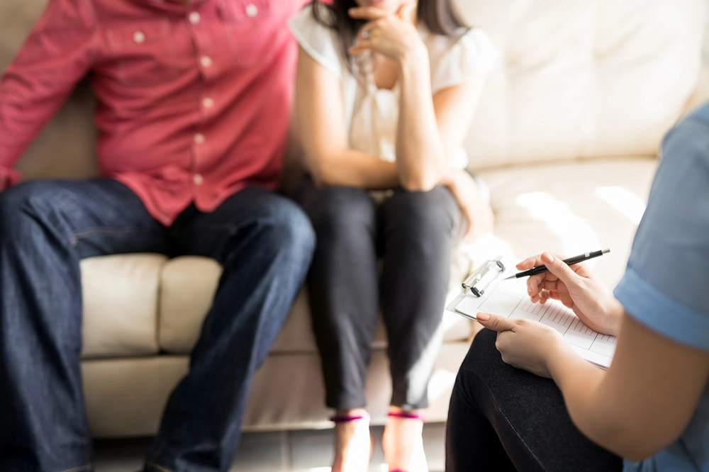 Couple sitting on a couch talking with a therapist taking notes