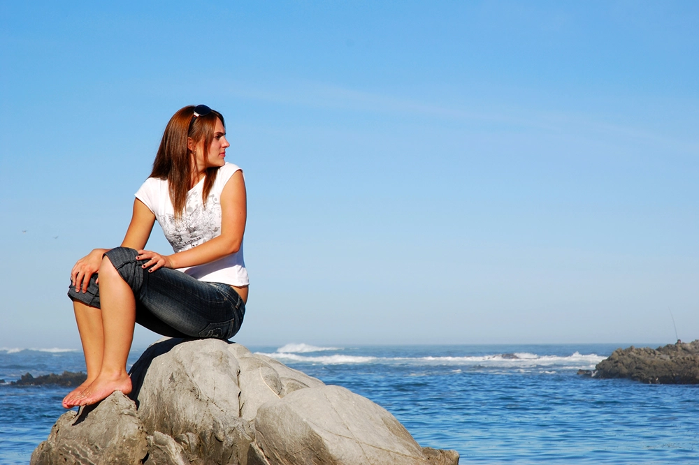 Woman sitting on rocks by the ocean looking out at the water