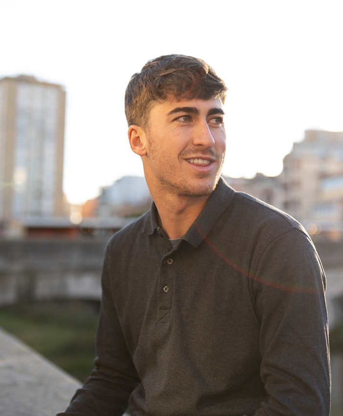 Young man smiling while looking to the side outdoors, representing confidence, optimism, and calm reflection