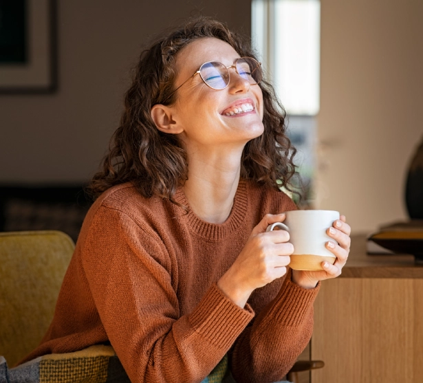 Smiling woman sitting indoors with a cup of coffee, enjoying a peaceful and relaxing moment