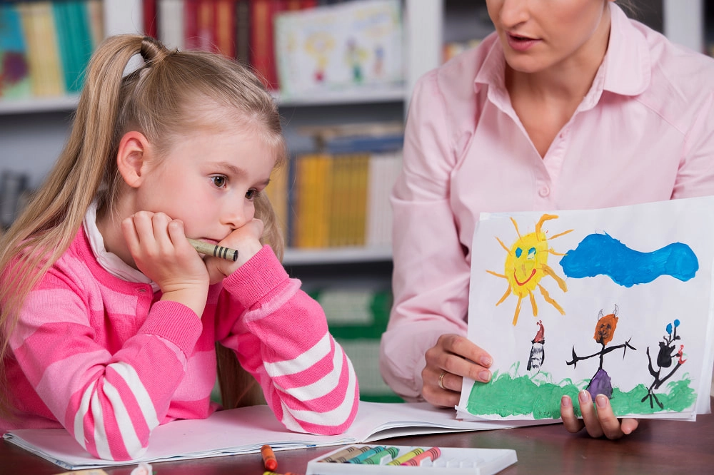 Child sitting with a therapist looking at a colorful drawing during play therapy