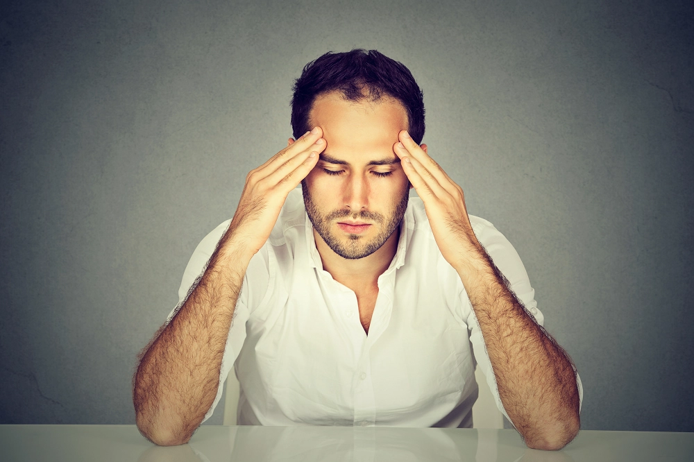 Man in a white shirt holding his temples with eyes closed, appearing stressed or in deep thought