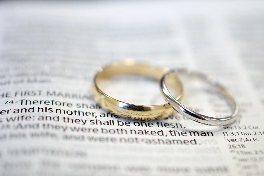 Two wedding rings placed on an open Bible page highlighting a verse about marriage