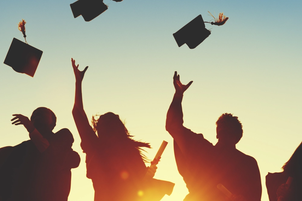 Silhouette of graduates celebrating by throwing caps in the air at sunset