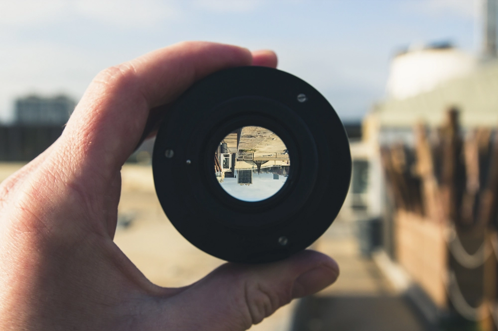 Person holding a camera lens showing an upside-down view of buildings and surroundings through the glass