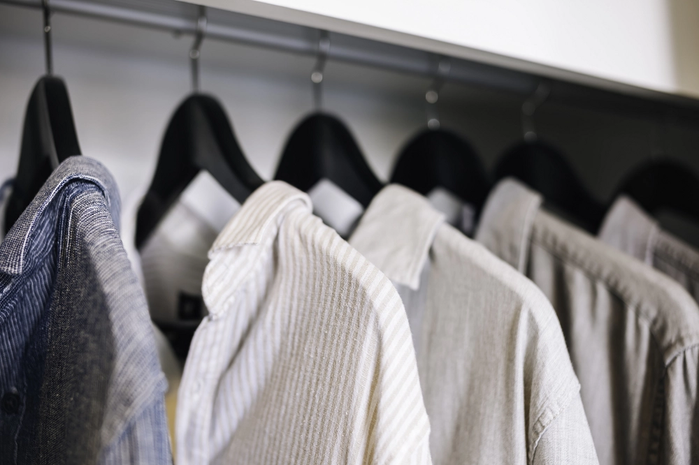 Neatly hung collared shirts in neutral tones on black hangers inside a closet