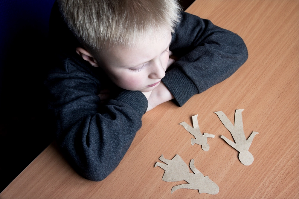 Sad boy looking at paper cutouts of a family on a wooden table