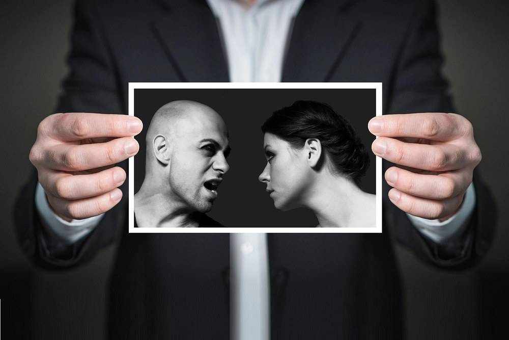 Person holding a photo showing a man angrily yelling at a woman who looks away in silence