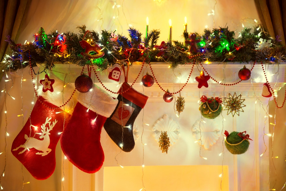 Christmas stockings hanging from a decorated mantel with garland, ornaments, and festive lights