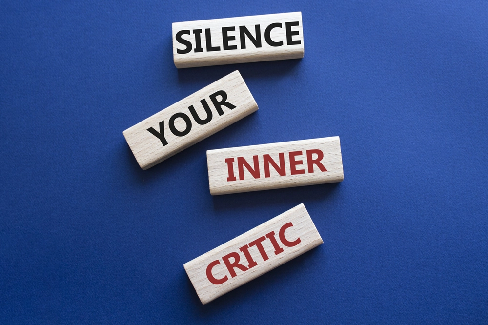 Wooden blocks on a blue background spelling out “Silence your inner critic"