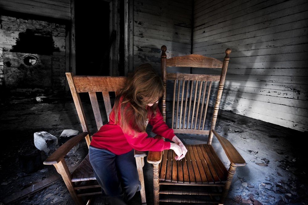 Sad girl in a red sweater sitting alone on a wooden chair in an abandoned room