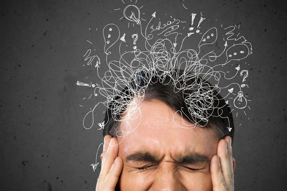Stressed man holding his head with chaotic scribble lines above symbolizing anxiety and racing thoughts