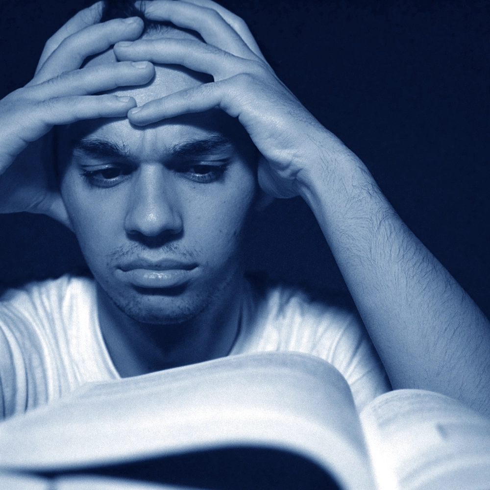 Man holding his head in his hands, appearing sad or stressed in a dimly lit blue-toned image