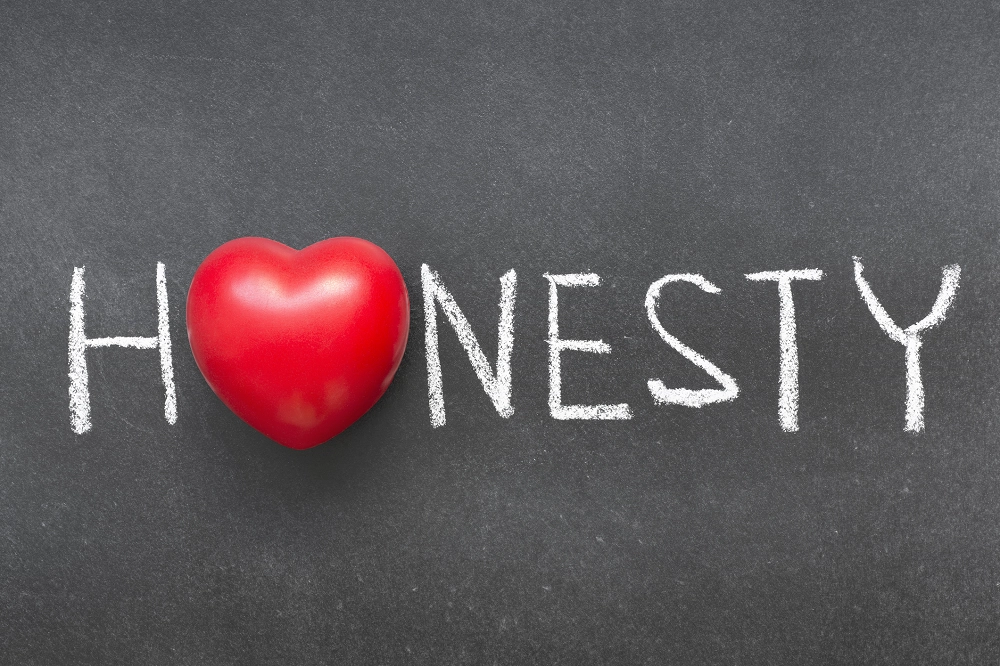 Word “Honesty” written in white chalk on a blackboard with a red heart replacing the letter O