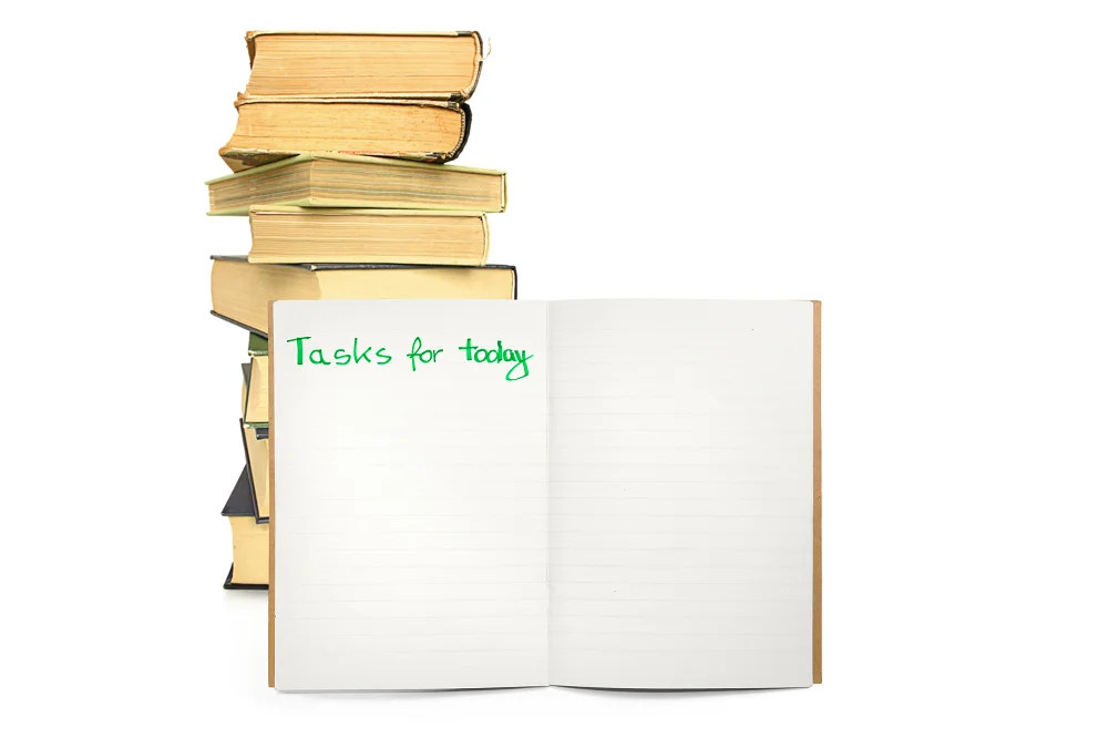 Open notebook with the words ‘Tasks for today’ written in green ink beside a stack of books on a white background