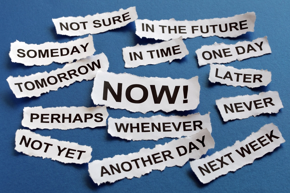 Paper scraps with words like “someday,” “tomorrow,” “later,” and a bold “NOW!” in the center on a blue background