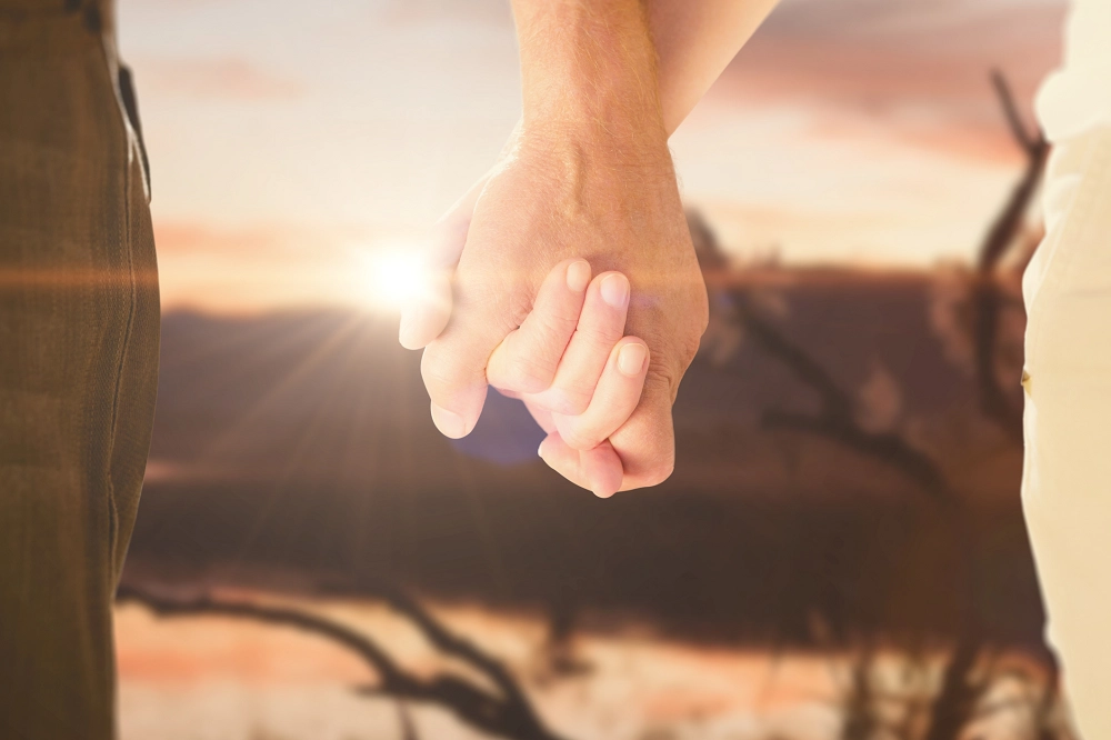 Close-up of two people holding hands with a warm sunset in the background, symbolizing love, connection, and togetherness