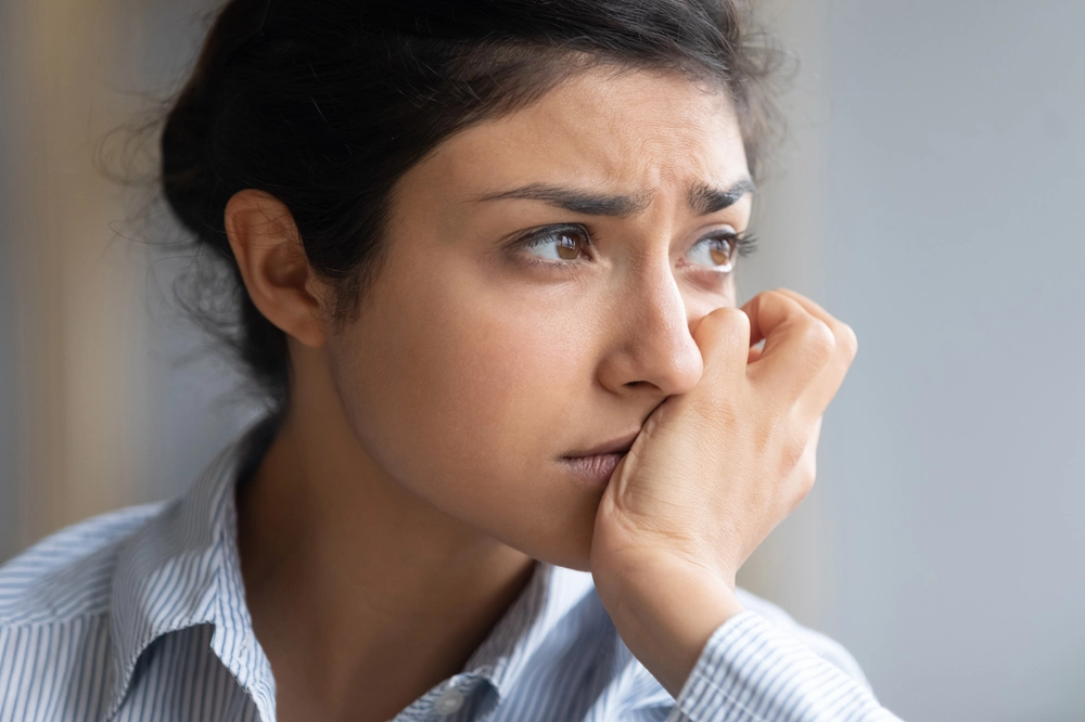 Woman looking out window with worried expression, appearing anxious or deep in thought
