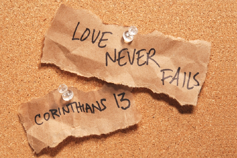 Two torn paper notes pinned to a corkboard with the handwritten Bible verse “Love never fails — Corinthians 13.”