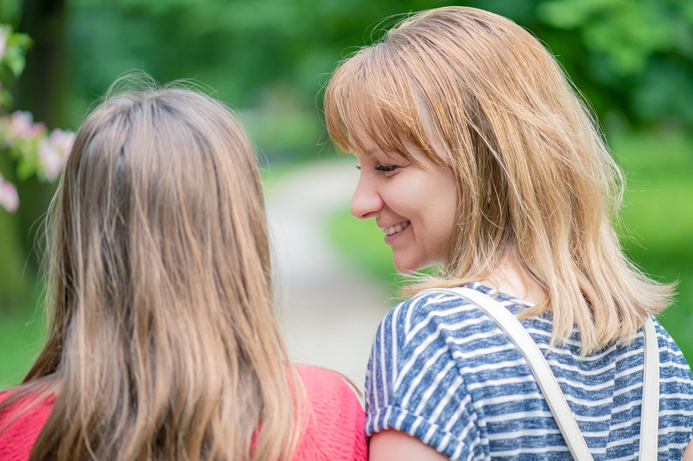 Smiling woman talking with a young girl while walking outdoors on a park path