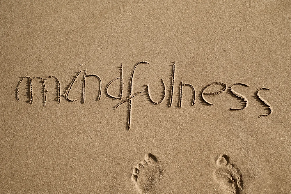 The word ‘mindfulness’ written in the sand with faint footprints below it