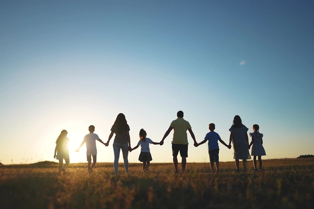 Large family holding hands while walking through a field at sunset, silhouetted against the sky