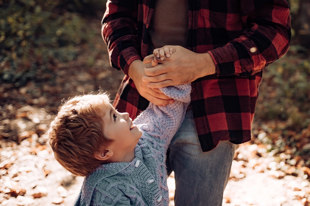 Smiling young boy holding an adult’s hands while looking up during a walk outdoors