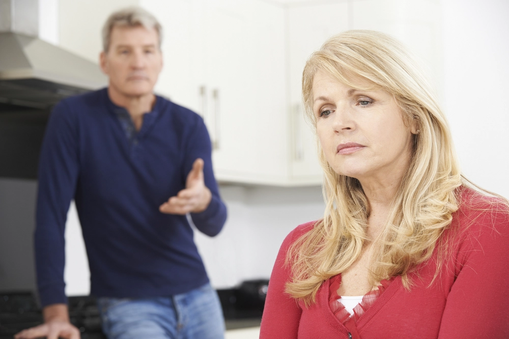 Middle-aged woman looking upset while a man in the background appears to be talking to her