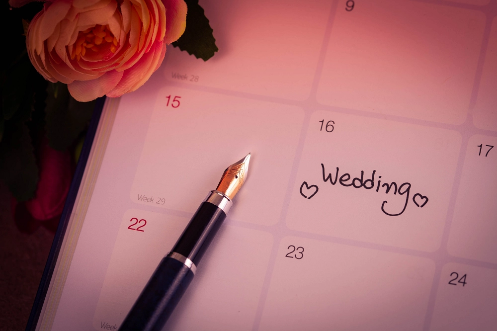 Close-up of a calendar with the word “Wedding” written on a date, next to a fountain pen and flowers
