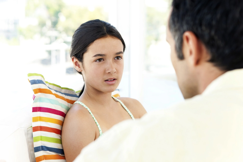 Teen girl sitting with a striped pillow, listening attentively to an adult during a serious conversation