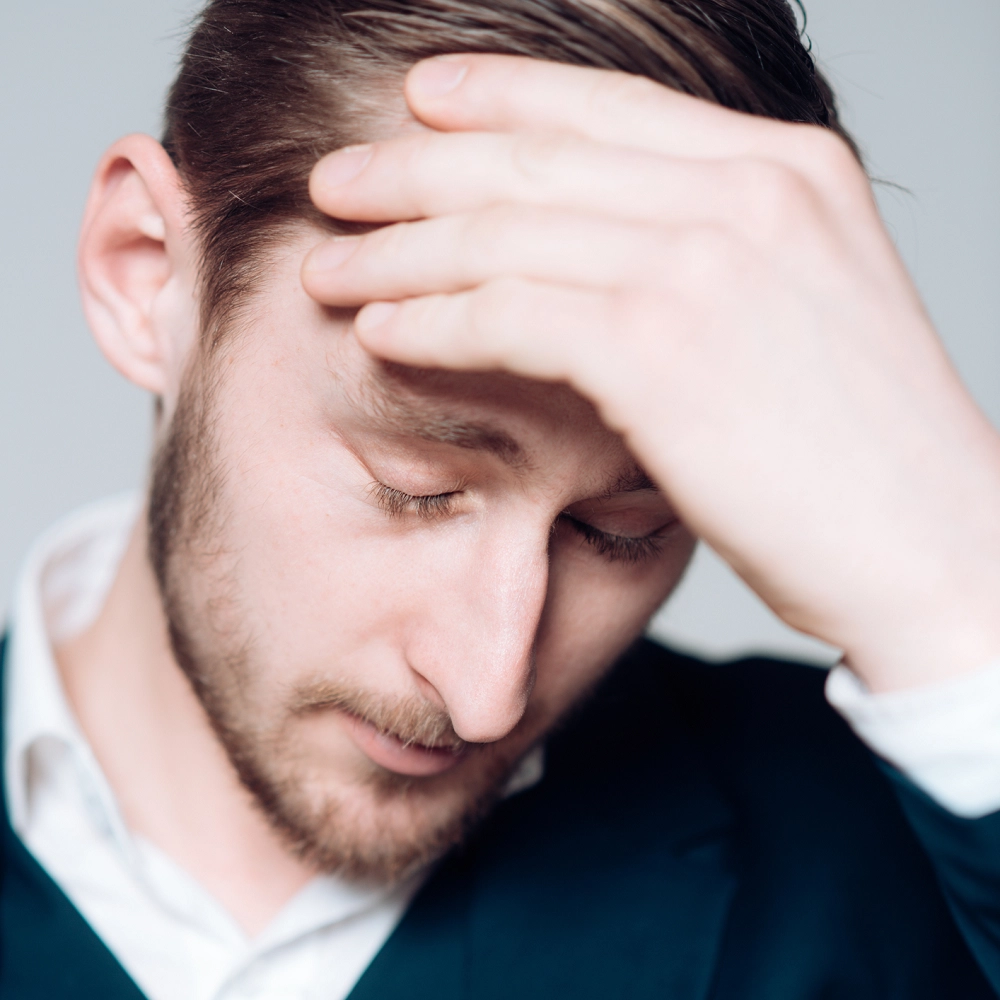 Close-up of a man with eyes closed and hand on his forehead, appearing stressed or upset