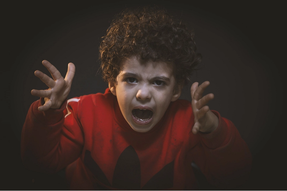 Young boy in a red shirt yelling with hands raised, expressing anger or frustration