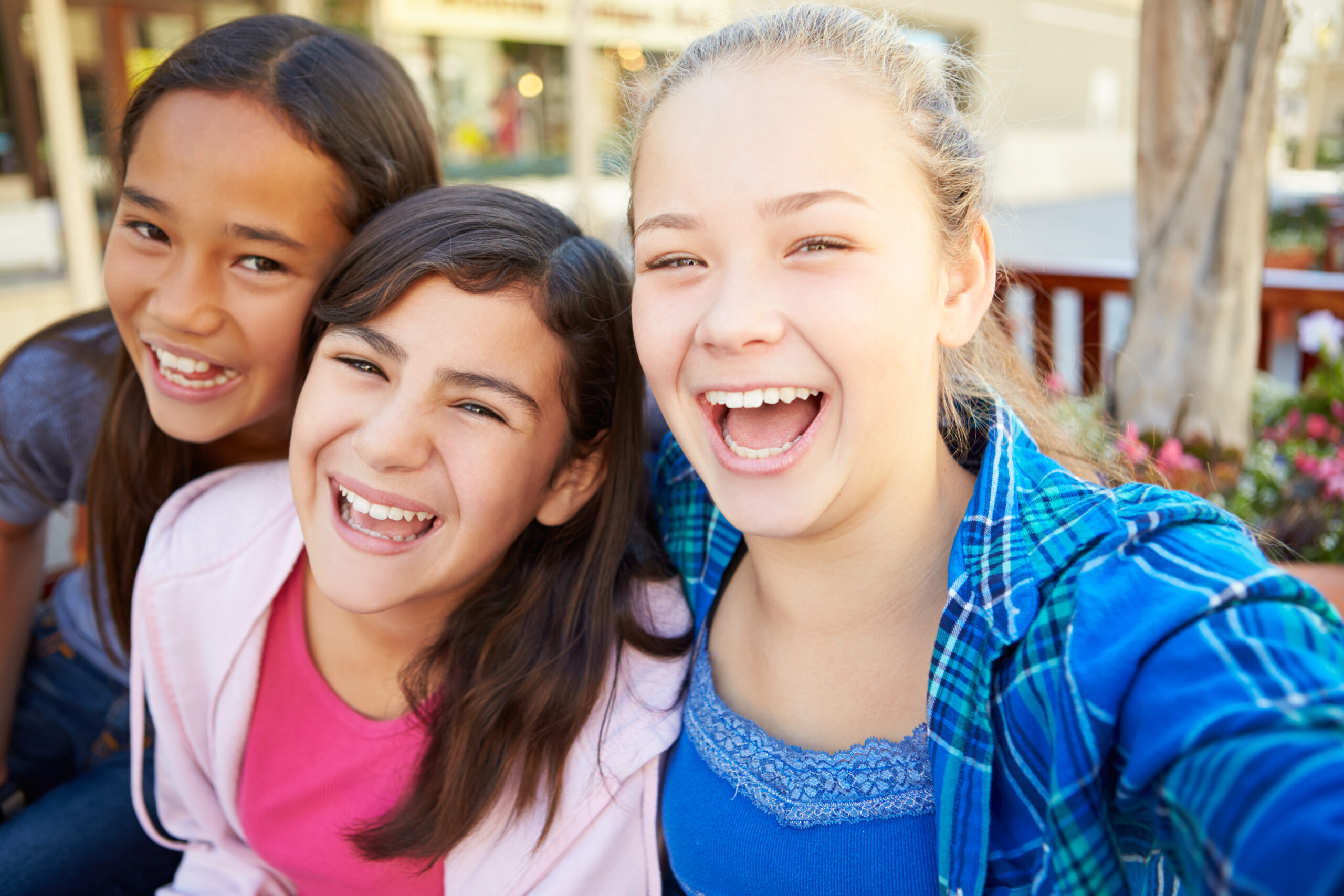 Three smiling preteen girls laughing together outdoors, showing friendship and happiness