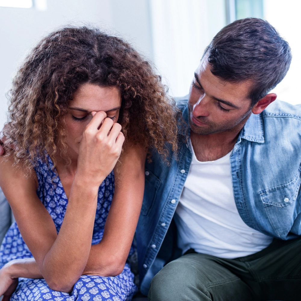 Man comforting a woman who looks upset and is holding her head in her hand