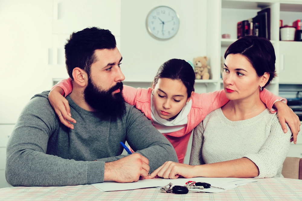Young girl hugging her parents as they sit together looking serious and thoughtful
