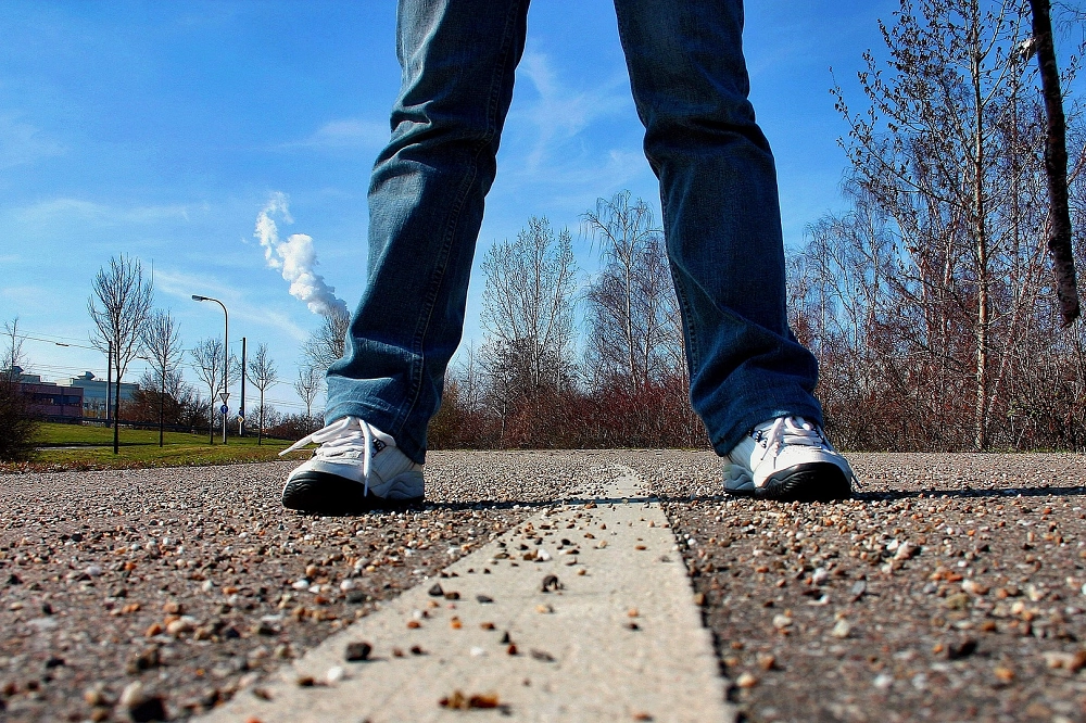 Person wearing jeans and white sneakers standing on a road with a painted center line outdoors