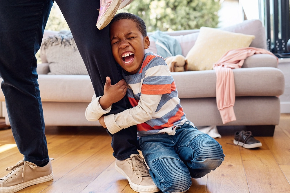 Laughing young boy hugging an adult’s leg playfully in a cozy living room