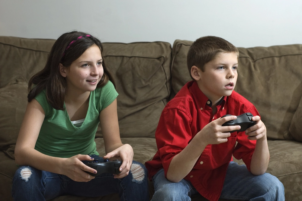 Boy and girl sitting on a couch playing video games with focused expressions
