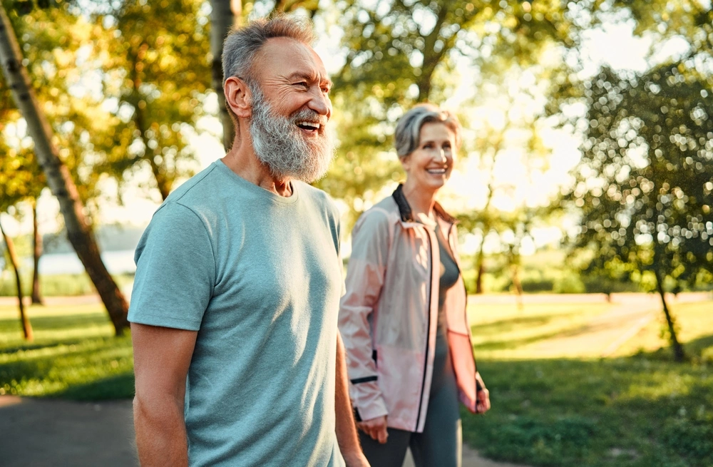 Smiling older couple walking together outdoors on a sunny day, enjoying a stroll through a park