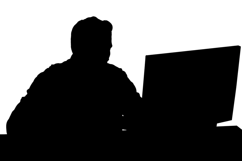 Silhouette of a person sitting at a desk using a computer against a white background