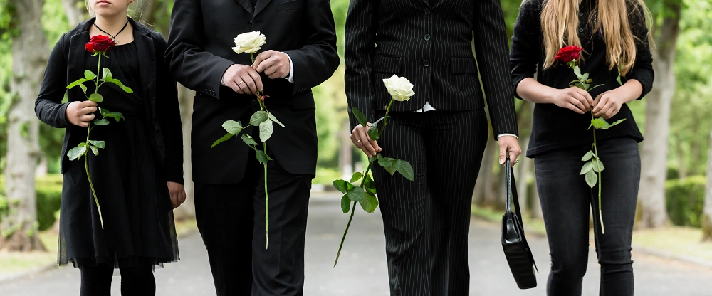 Family dressed in black walking together holding roses at a funeral or memorial service