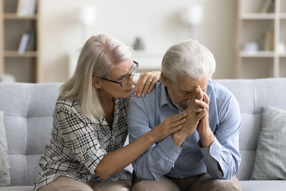 Concerned older woman comforting her distressed partner while sitting together on a couch