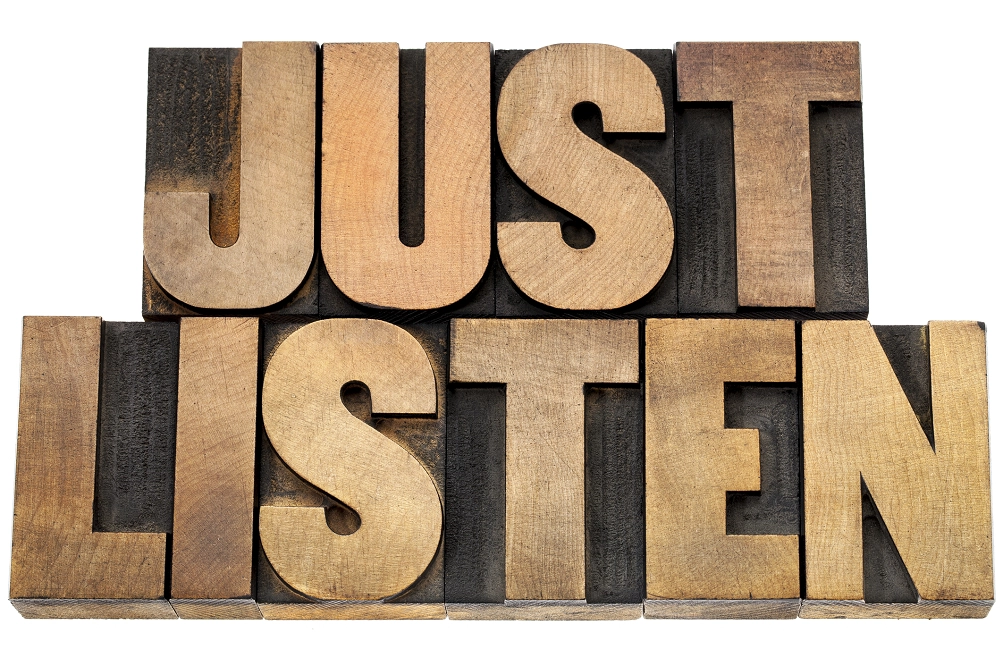 Wooden block letters spelling the words “Just Listen” on a white background